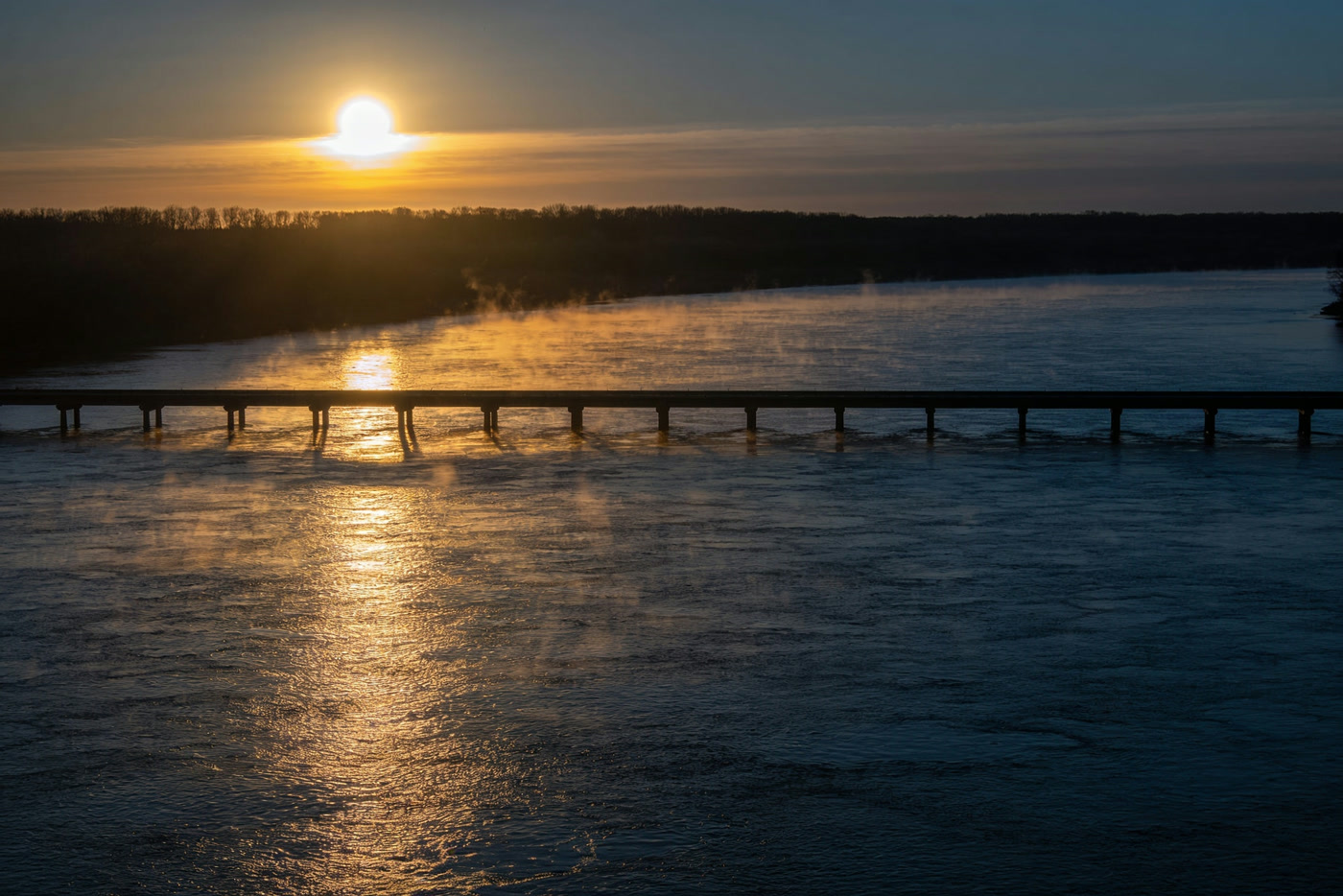 Sunrise laying a band of gold across the river beside a low causeway bridge